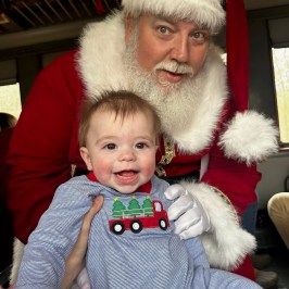 Santa holding a smiling baby aboard the Summerville Santa Special holiday train.
