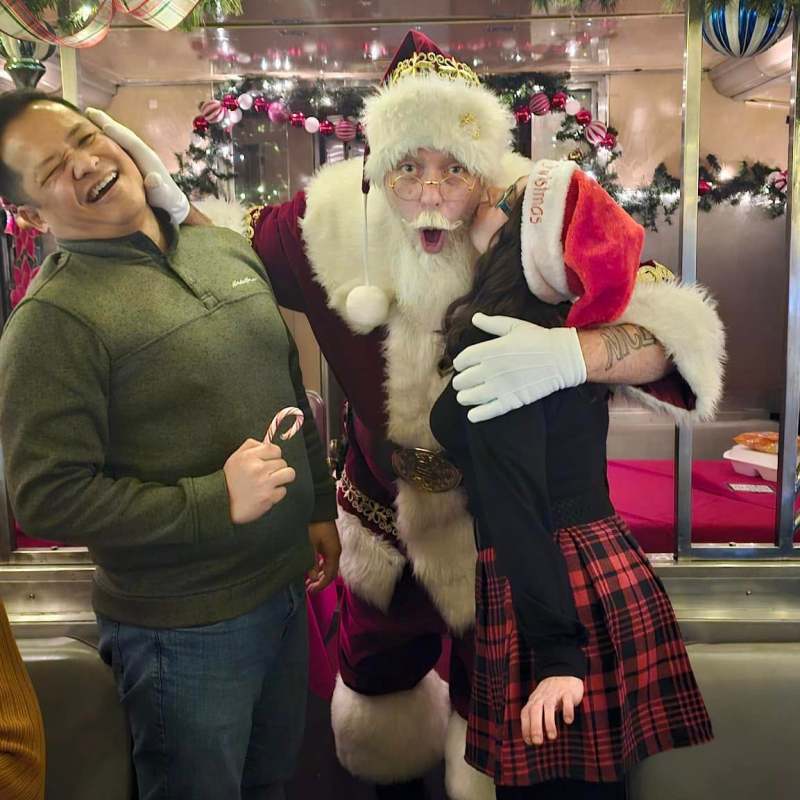 Santa laughing with a guest and child aboard the NightCaps With St. Nick holiday train.