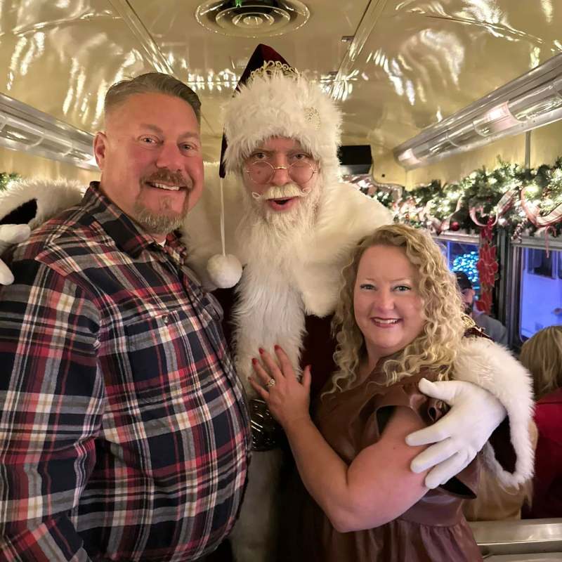 Smiling father and daughter posing with Santa aboard the NightCaps holiday train
