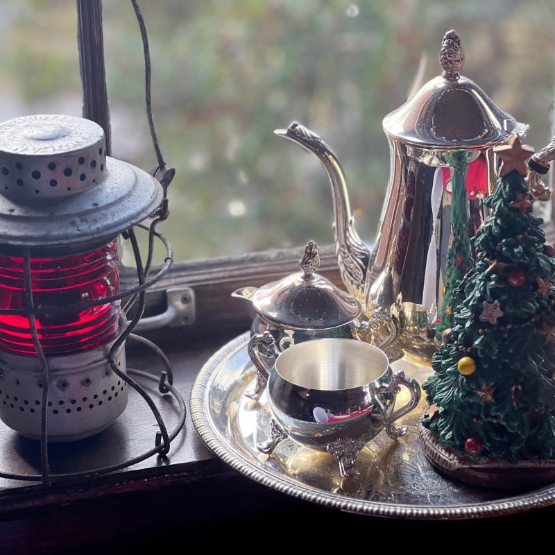 Vintage lantern and silver tea set beside a ceramic Christmas tree on a train windowsill.