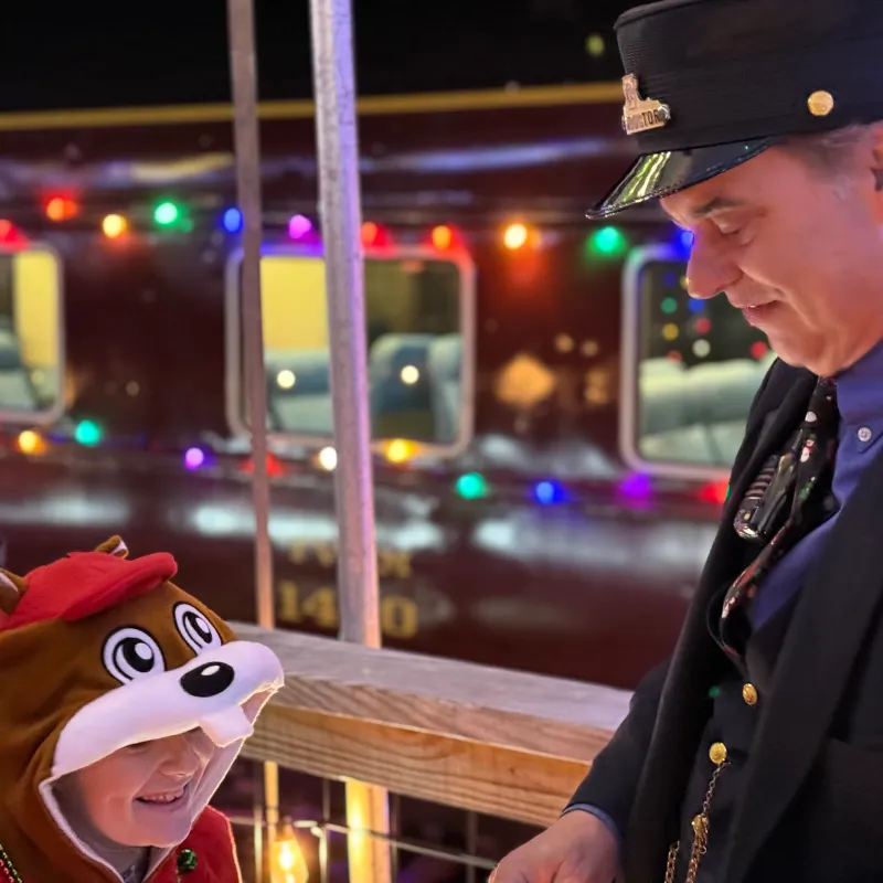 TVRM train conductor smiling with a child aboard a decorated holiday train