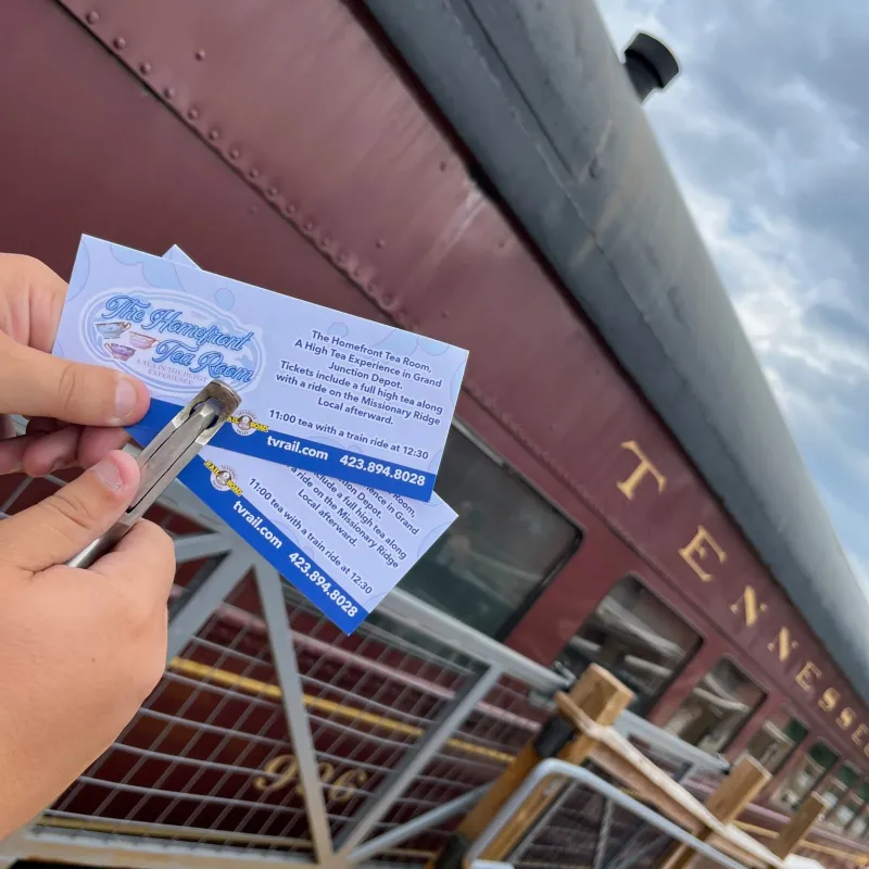Hands punching tickets near a vintage train car at the Chattanooga depot.