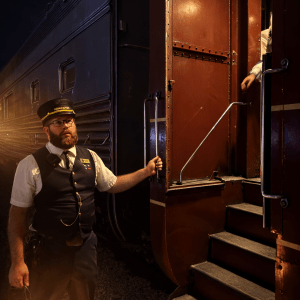 TVRM conductor holding a lantern beside a vintage train door during nighttime boarding in Chattanooga