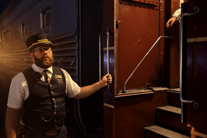 TVRM conductor holding a lantern beside a vintage train door during nighttime boarding in Chattanooga