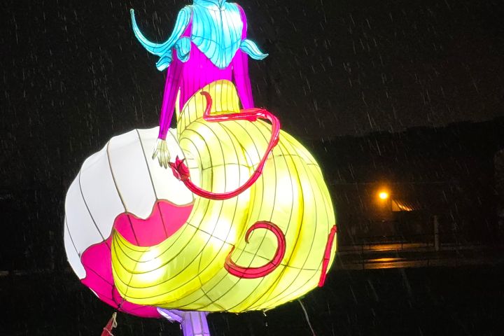 Illuminated mushroom-shaped lantern with human face in rain at night.