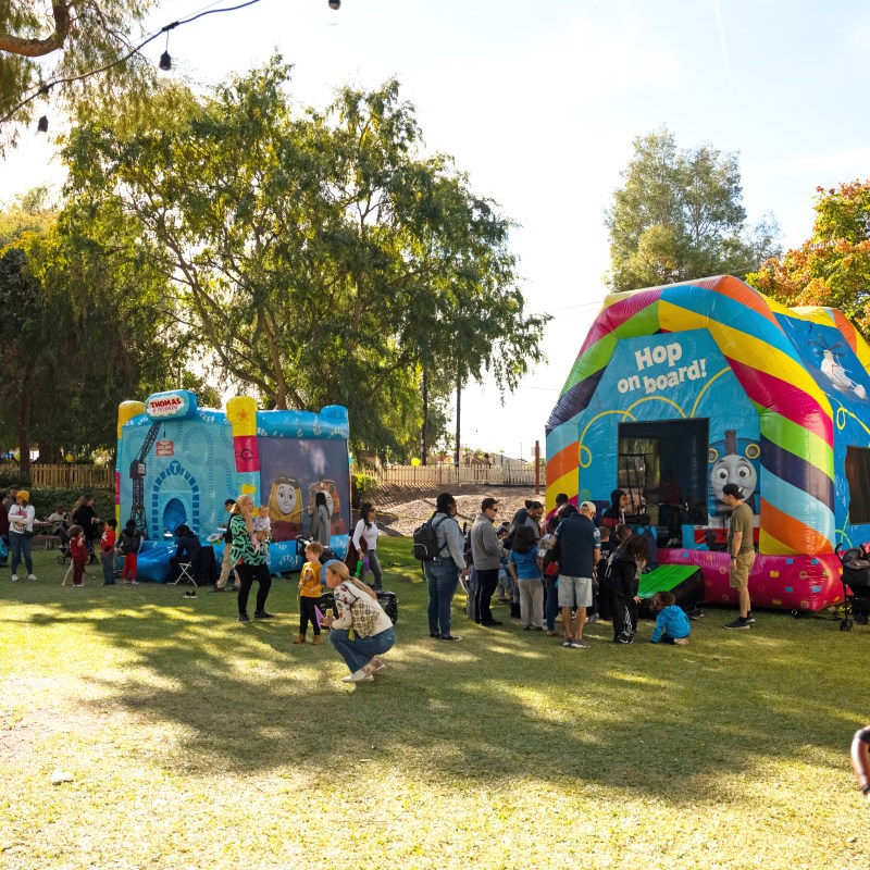 People at an outdoor event with inflatable bounce houses and trees.