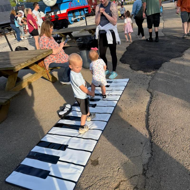 Kids playing on a large piano mat outdoors near a Thomas the Tank Engine train.