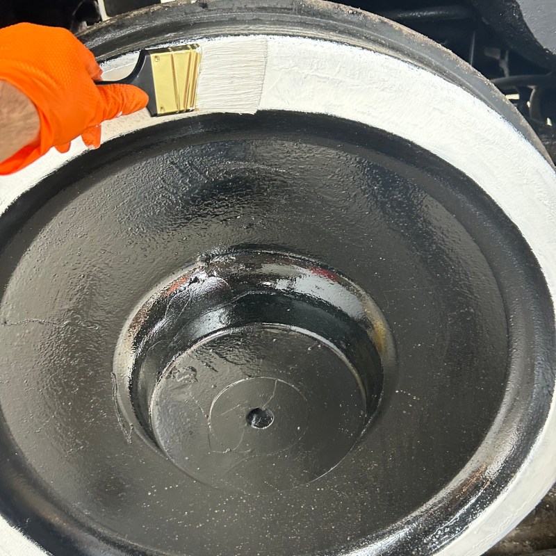 Person painting a large, black wheel's rim white with a brush.