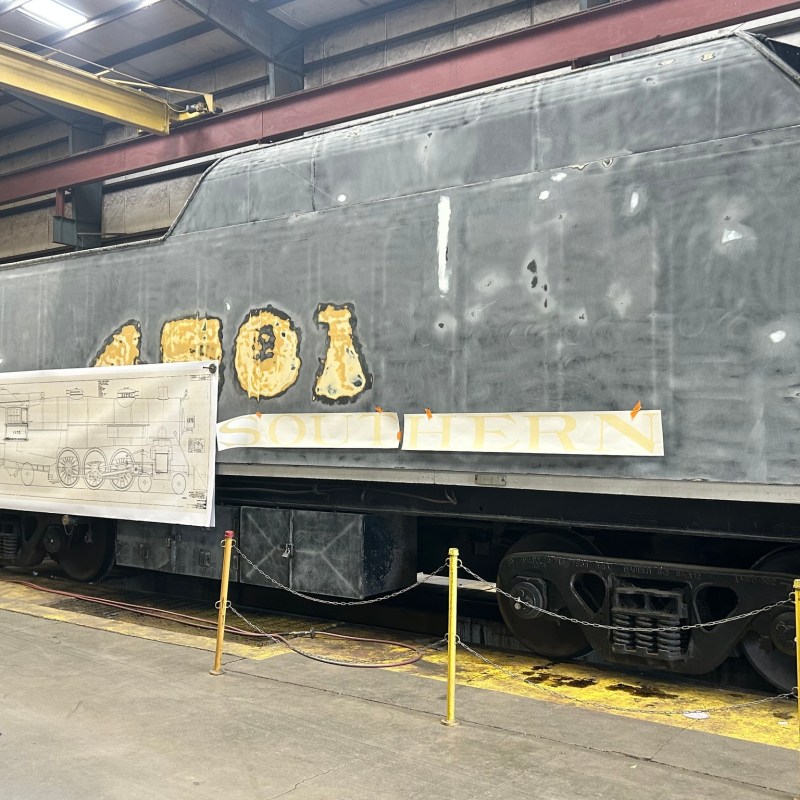 Partially restored train engine in a workshop with a blueprint on display.